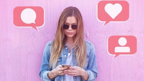 Une jeune femme en veste en jean posant devant un fond rose et utilisant son téléphone portable