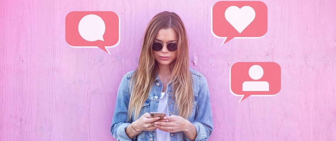Quels influenceurs choisir pour optimiser sa campagne en ligne ? Une jeune femme en veste en jean posant devant un fond rose et utilisant son téléphone portable