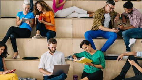 un groupe de gens assis sur une estrade de bois en train de regarder leur portable.