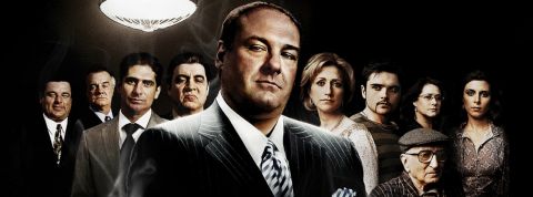 Les Soprano, meilleure série du siècle un homme habillé en mafieux avec ses acolytes en arrière plan.