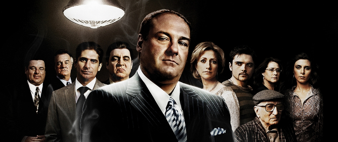 Les Soprano, meilleure série du siècle un homme habillé en mafieux avec ses acolytes en arrière plan.