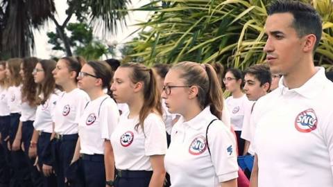 une jeune influenceur au garde à vous dans la jungle avec d'autres jeunes.