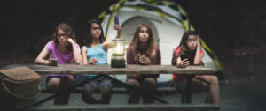 quatre jeunes filles assises à une table de camping qui regardent leur téléphone.