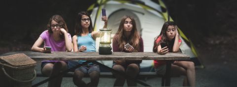 Les réseaux sociaux secrets des ados quatre jeunes filles assises à une table de camping qui regardent leur téléphone.