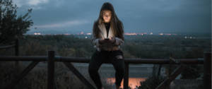 une jeune fille assise sur une barrière qui regarde son téléphone.