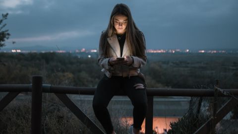 une jeune fille assise sur une barrière qui regarde son téléphone.