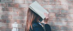 jeune femme masquant son visage avec un cahier