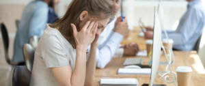 Une jeune femme se prenant la tête entre les mains derrière son écran d'ordinateur au bureau
