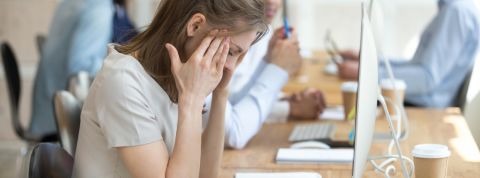 Les jeunes dépriment au travail Une jeune femme se prenant la tête entre les mains derrière son écran d'ordinateur au bureau