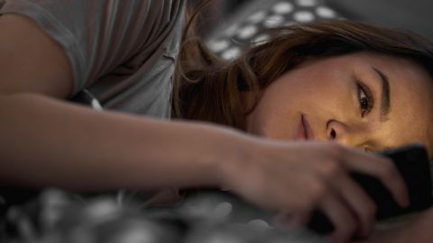 une jeune fille allongée dans un lit qui regarde un smartphone