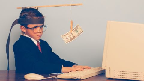 Petit garçon devant un ordinateur, tenté par un billet accroché devant ses yeux.