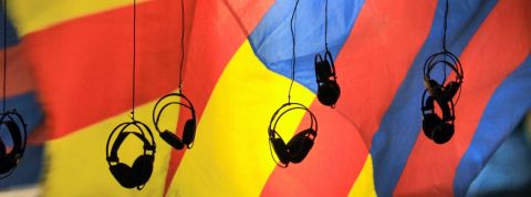 Le podcast vole au secours des reportages écrit Des casques audio suspendu dans le vide avec un drat jaune rouge et bleu en arrière plan.