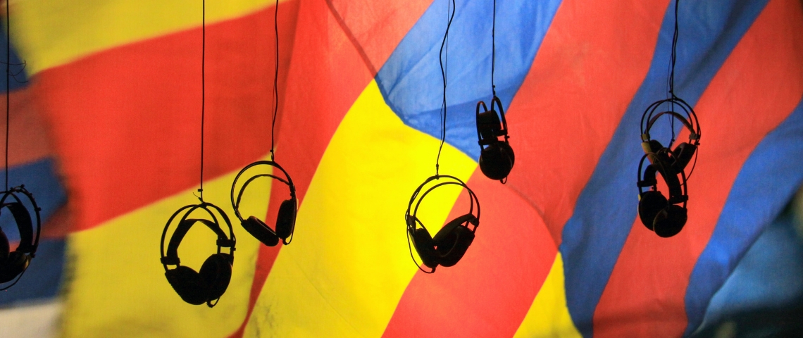 Le podcast vole au secours des reportages écrit Des casques audio suspendu dans le vide avec un drat jaune rouge et bleu en arrière plan.