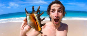 Un jeune homme sur une plage en train de tenir un coquillage
