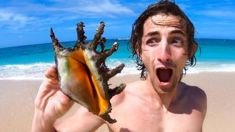 Un jeune homme sur une plage en train de tenir un coquillage