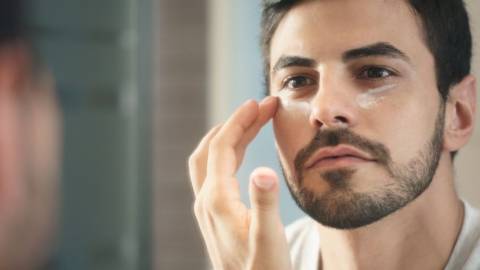 Un homme qui met de la crème sous ses yeux devant un mirroir