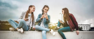 Trois jeunes filles sur un mur en train de regarder leur portable