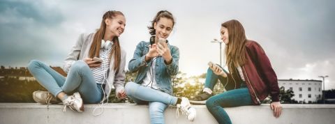 Sur Snapchat, les marques doivent miser sur la sincérité et la proximité Trois jeunes filles sur un mur en train de regarder leur portable