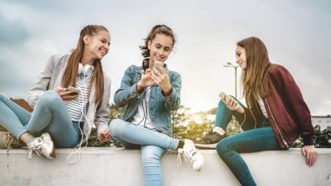 Trois jeunes filles sur un mur en train de regarder leur portable