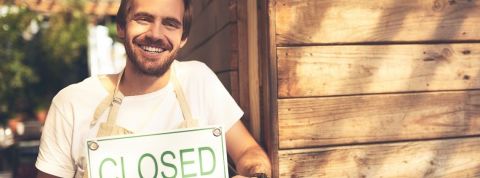 Ces entreprises qui boycottent le Black Friday (et qui y gagnent) Un jeune homme souriant tient une pancarte de boutique - fermé -