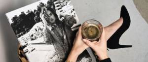 Une femme lit son magazine en tenant un café noir et porte des talons noirs