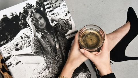 Une femme lit son magazine en tenant un café noir et porte des talons noirs