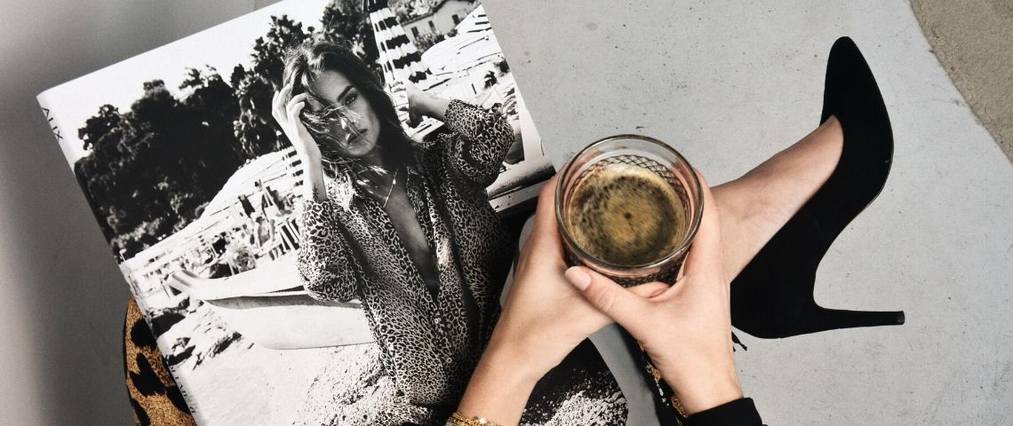 Comment garder un média d’avance ? Une femme lit son magazine en tenant un café noir et porte des talons noirs