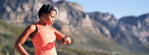 Google rachète Fitbit : pourquoi les GAFA veulent nous soigner ? Femme en tenue de sport regarde son bracelet connecté dans la montagne.