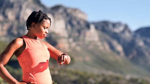 Femme en tenue de sport regarde son bracelet connecté dans la montagne.