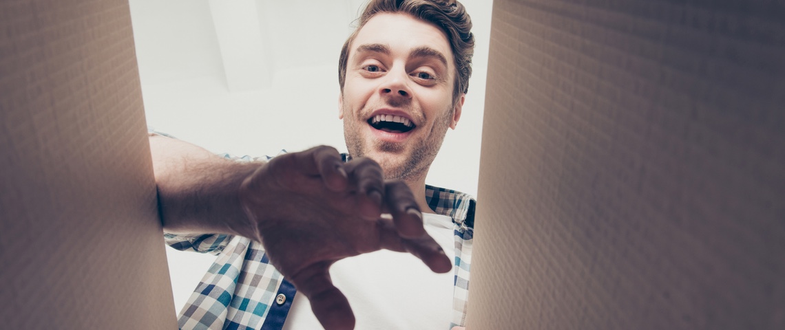 Wish : pourquoi ce bazar du web, loin de la consommation responsable, cartonne Homme vue contre-plongée en train d'ouvrir un colis en carton.