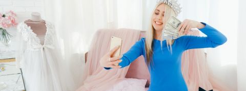 Les influenceurs vont-ils faire exploser la bulle ? une jeune fille blonde avec une couronne sur la tête se prend en photo avec une liasse de billets dans la main.
