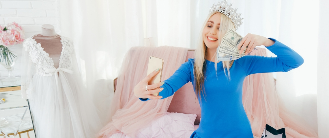 Les influenceurs vont-ils faire exploser la bulle ? une jeune fille blonde avec une couronne sur la tête se prend en photo avec une liasse de billets dans la main.
