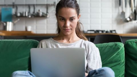 Une femme qui regarde son écran d'ordinateur assise sur son canapé