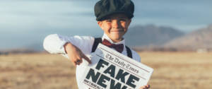 un enfant dans un champs qui tient un journal avec écrit fake news dessus