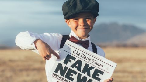 un enfant dans un champs qui tient un journal avec écrit fake news dessus