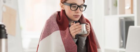 Pourquoi a-t-on du mal à travailler en hiver ? Une jeune femme emmitouflée dans un plaid derrière son ordinateur