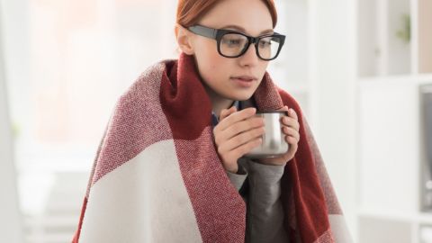 Une jeune femme emmitouflée dans un plaid derrière son ordinateur
