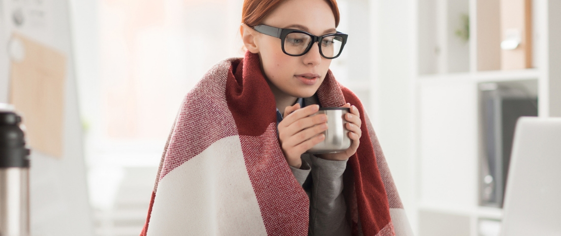 Pourquoi a-t-on du mal à travailler en hiver ? Une jeune femme emmitouflée dans un plaid derrière son ordinateur