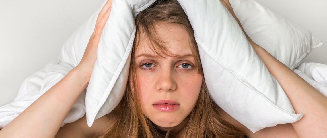 Penser moins pour dormir plus Une femme insomniaque qui tient sa tête entre deux oreillers