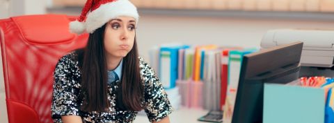 Noël au bureau, comment ça se passe ? Une femme assise à son bureau, portant un bonnet de père noël, en train de s'étirer