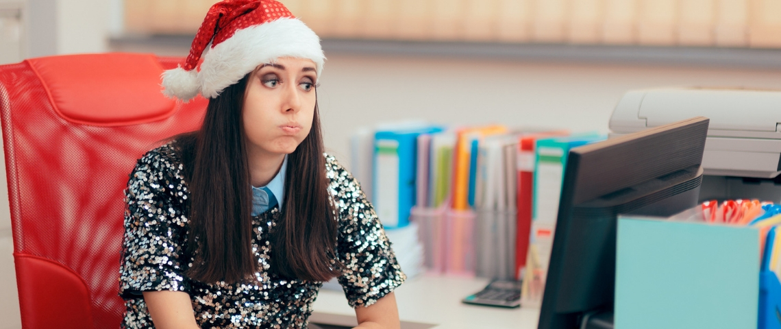 Noël au bureau, comment ça se passe ? Une femme assise à son bureau, portant un bonnet de père noël, en train de s'étirer