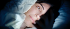 Une femme regarde son smartphone dans son lit
