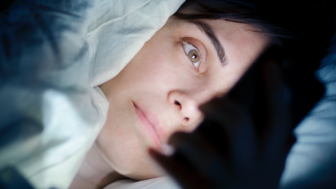 Une femme regarde son smartphone dans son lit
