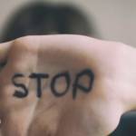 un enfant montre la paume de sa main où est écrit en noir le mot stop