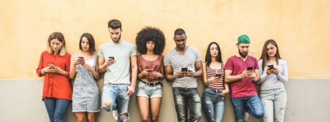 Tinder, Happn et Grindr partagent leurs données utilisateurs. Un groupe de jeunes adossés à un mur jaune consultent leur smartphone.