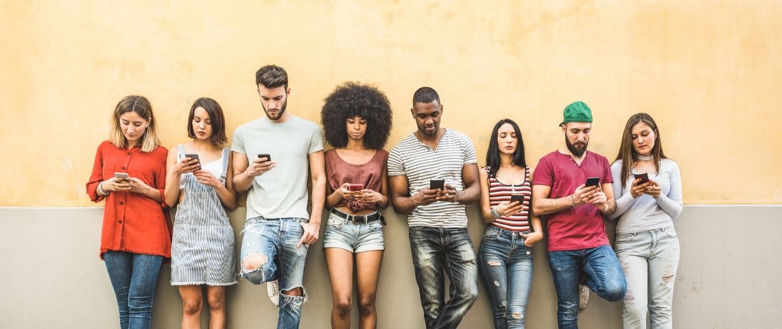 Tinder, Happn et Grindr partagent leurs données utilisateurs. Un groupe de jeunes adossés à un mur jaune consultent leur smartphone.