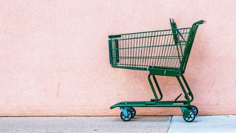Un chariot de supermarché vert abandonné devant un mur rose