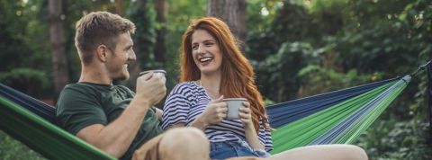 Le dating s'adapte au changement climatique Un couple dans la forêt en train de prendre un café sur un hamac