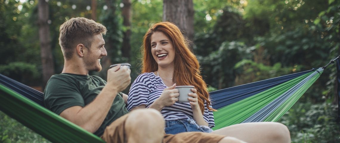 Le dating s'adapte au changement climatique Un couple dans la forêt en train de prendre un café sur un hamac