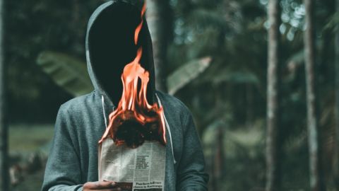 un homme à capuche dans une forêt tient un journal en feu